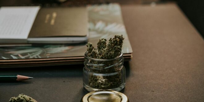 A close-up image of cannabis buds in a glass container on a desk, emphasizing a natural and relaxed setting.