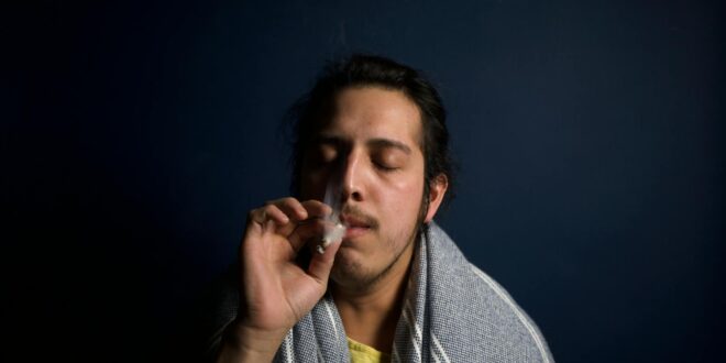 Close-up of a young man comfortably smoking in a dimly lit room, reflecting relaxation.